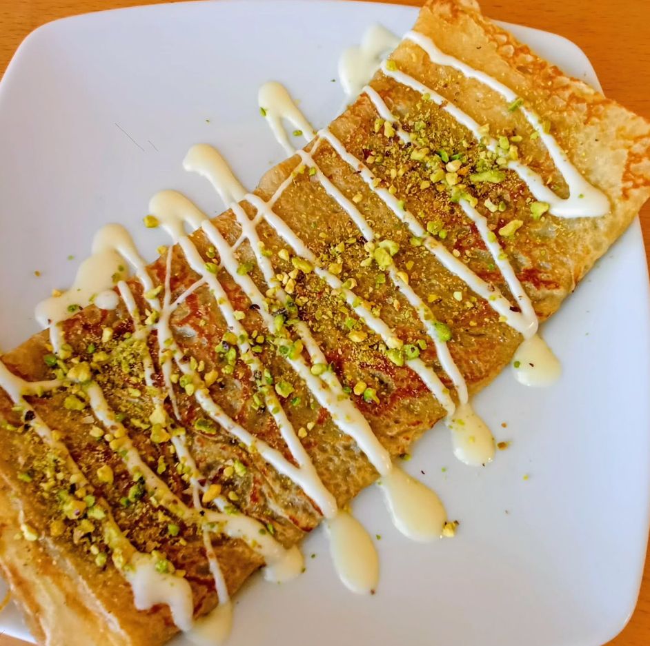 Crêpe on a white plate with white sauce and chopped pistachio