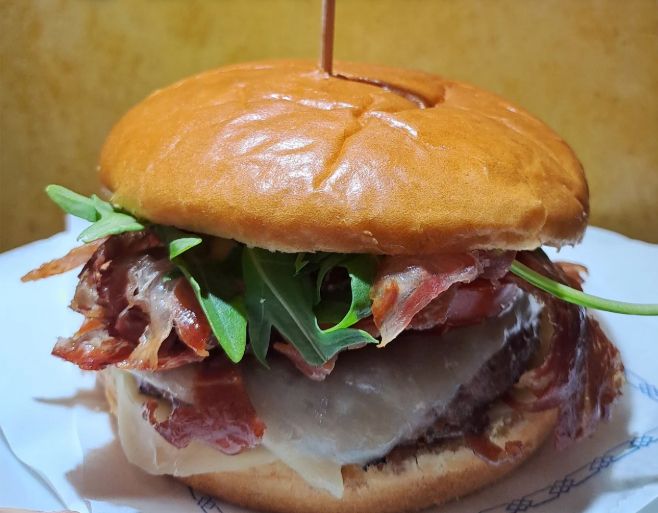 Burger on a brioche bun with cured ham, cheese and rocket