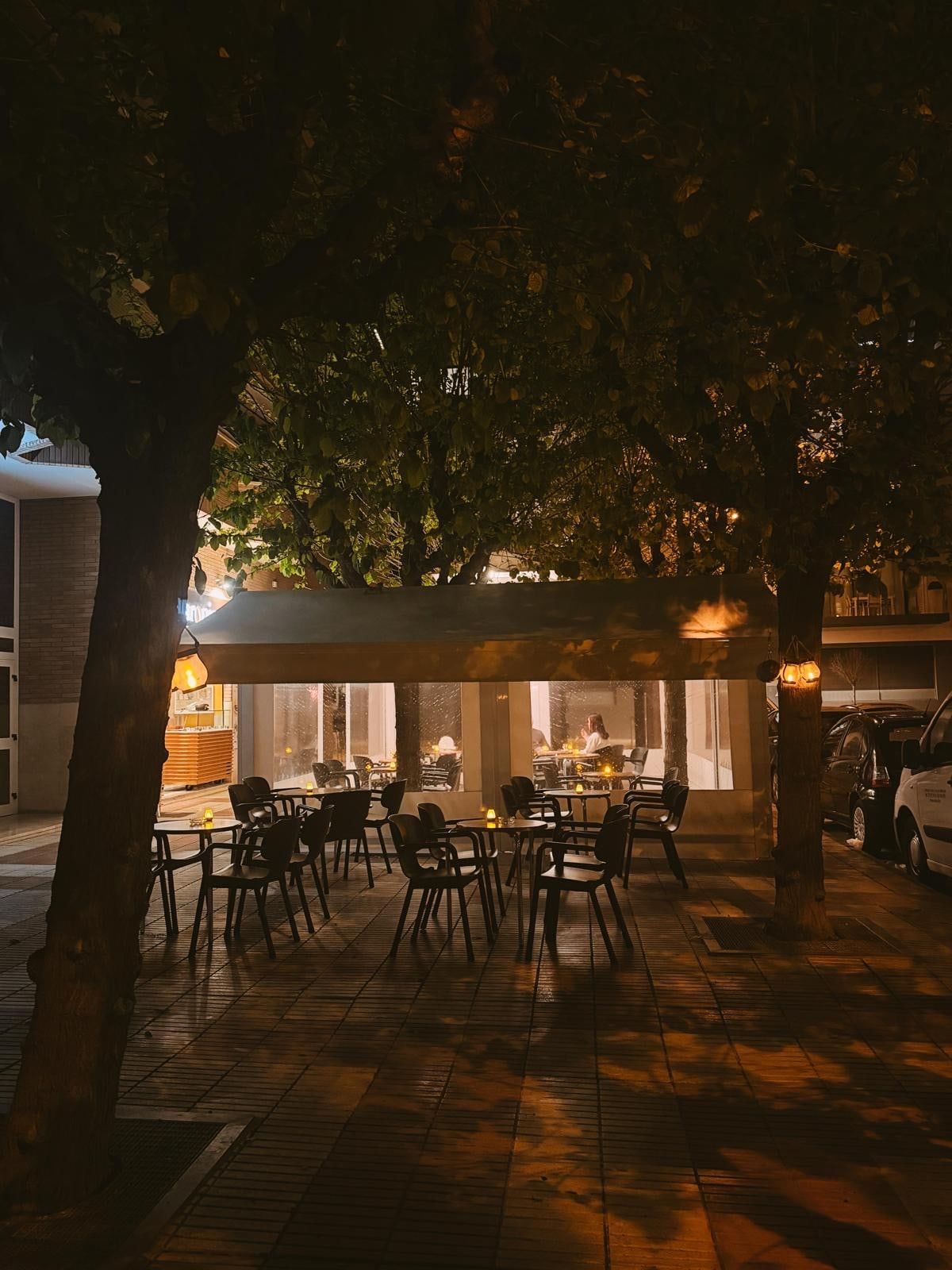 The terrace at dusk under the trees, with candles on the tables and the café lit up behind
